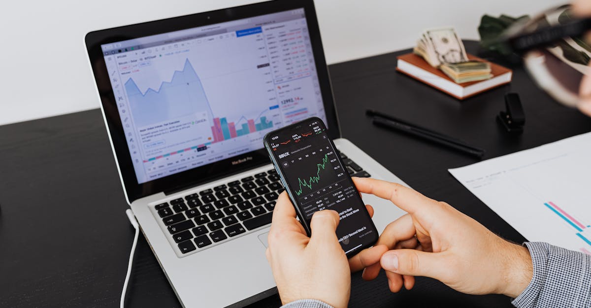 Person analyzing stock market data on a laptop and smartphone indoors.
